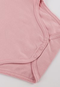 Light pink cotton bodysuit with a round neckline, snap fasteners, and soft texture. Features curved edges and stitched detailing.