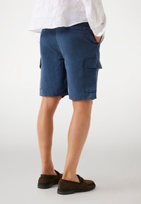 Shorts cargo bleu marine en tissu texturé, avec des poches latérales et une coupe décontractée, associés à des chaussures à enfiler marron.
