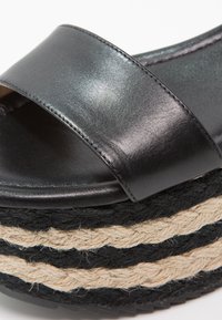 Sandale plateforme en cuir noir avec large bride et semelle en jute tissée noire et naturelle à motif rayé.