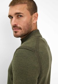 Grüner Strickpullover mit hohem Kragen, gerippter Textur und Kontrastnähten. Hat eine figurbetonte Form und eine glatte Oberfläche.