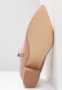 Bottine beige en daim à bout pointu avec talon bloc texturé et fermeture éclair latérale, vue de la semelle et du talon sur fond blanc.