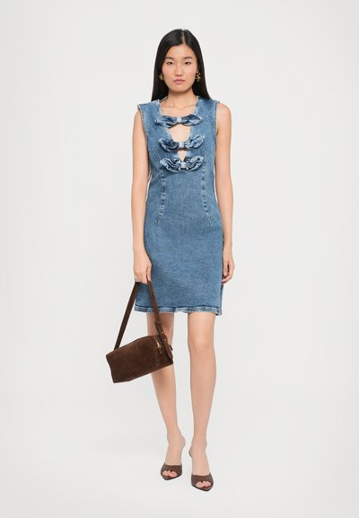 Denim mekko, jolla on vartalonmyötäinen siluetti, hihattomat hihat ja kolme rypytettyä kangaskoristetta rinnassa. Yhdistetty ruskean mokkanahan käsilaukun ja jalkineiden kanssa.