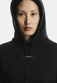 Schwarzer Kapuzenpullover mit Zugband, ausgestattet mit einem "SWISS ENGINEERING"-Label auf der Brust. Glatte Textur und minimalistisches Design.