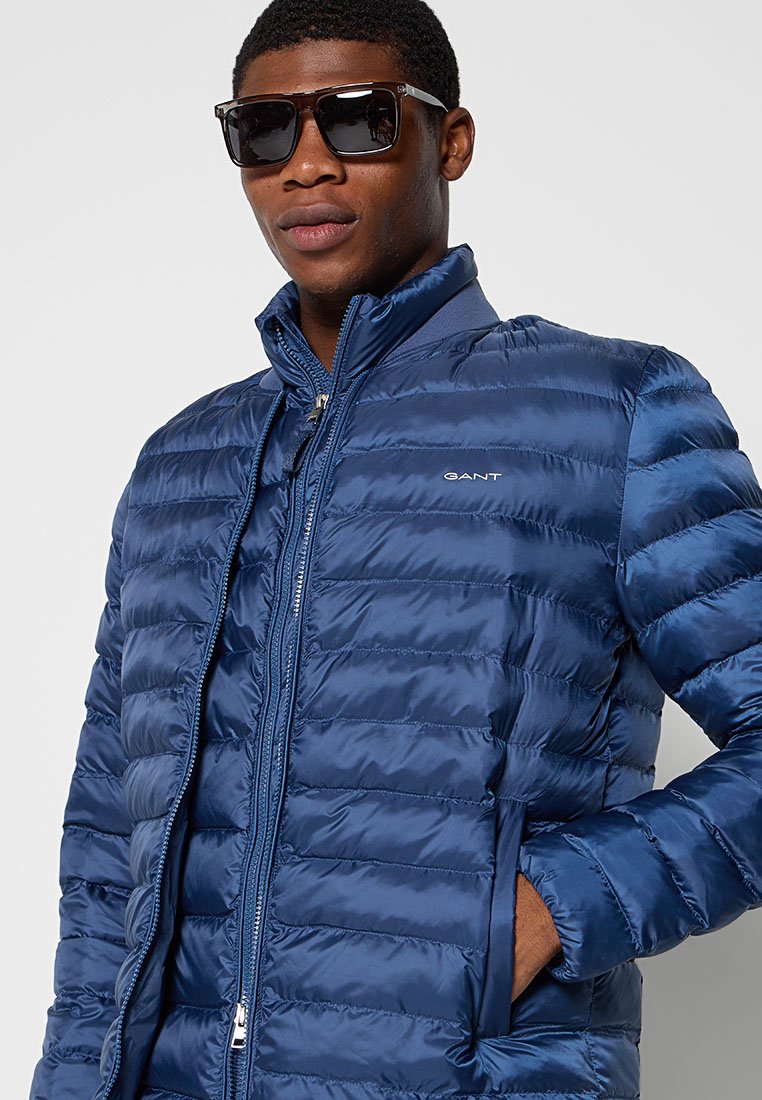 Granatowa pikowana kurtka z zamkiem z przodu, stojącym kołnierzem i kieszeniami. Lekki materiał z poziomym przeszyciem i detalem logo.