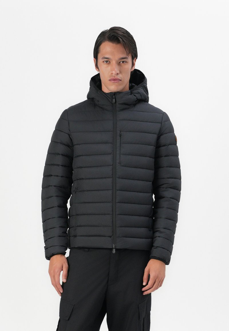 Sort pufferjakke med quiltet design, hætte, frontlynlås og en lille lynlåslomme. Tekstureret stof og elastiske manchetter.