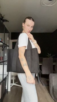 Svart totebag med brede stoffstropper, rektangulær form og glidelås-lukking, plassert mot en mørk bakgrunn. Teksturert stoff.
