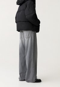 Sort pufferjakke med hætte, parret med løse, lysegrå denimbukser og sorte ankelstøvler. Casual, oversized silhuet.