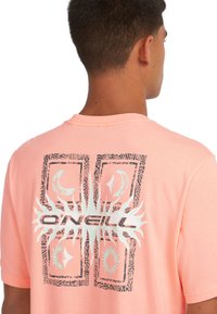 Lys rosa kortærmet t-shirt med et grafisk print, der viser sorte og teal sol- og månedesigns, samt "O'Neill" tekst i fede sorte bogstaver.