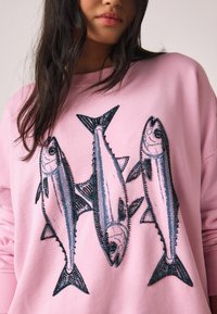 Roze sweatshirt met een geborduurd ontwerp van drie vissen in donkerblauw. Het materiaal is zacht, met een losse pasvorm en een ronde hals.