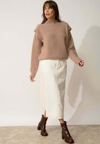 Beige gebreide trui met hoge hals, gecombineerd met een crèmekleurige midi-rok en bruine blokhak enkellaarsjes. Geweven stof en naden zichtbaar.