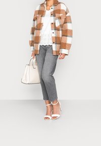 Hnědo-bílý kostkovaný oversized kabát přes bílý top se scalloped lemem, šedé džíny, bílé lodičky na kotníku a strukturovaná béžová kabelka.
