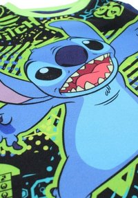 Chemise bleu à manches courtes présentant un graphisme d'un personnage aux grands yeux, dents aiguisées et accents vert néon sur un fond sombre.