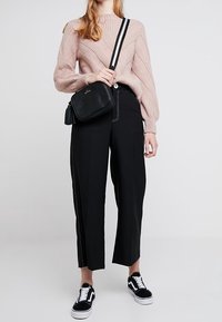 Lys rosa strikket sweater med et tekstureret zigzag-mønster, parret med brede sorte bukser. En sort crossbody taske og sorte sneakers fuldender outfittet.