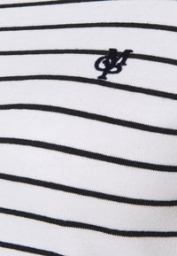 Tela blanca con rayas negras horizontales. Presenta un pequeño logo bordado en navy. Textura suave, diseño casual, material ligero.