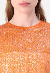Oranje pailletten top met een doorzichtige textuur. Ronde halslijn en korte mouwen, met een patroon van kleine, reflecterende schijfjes.