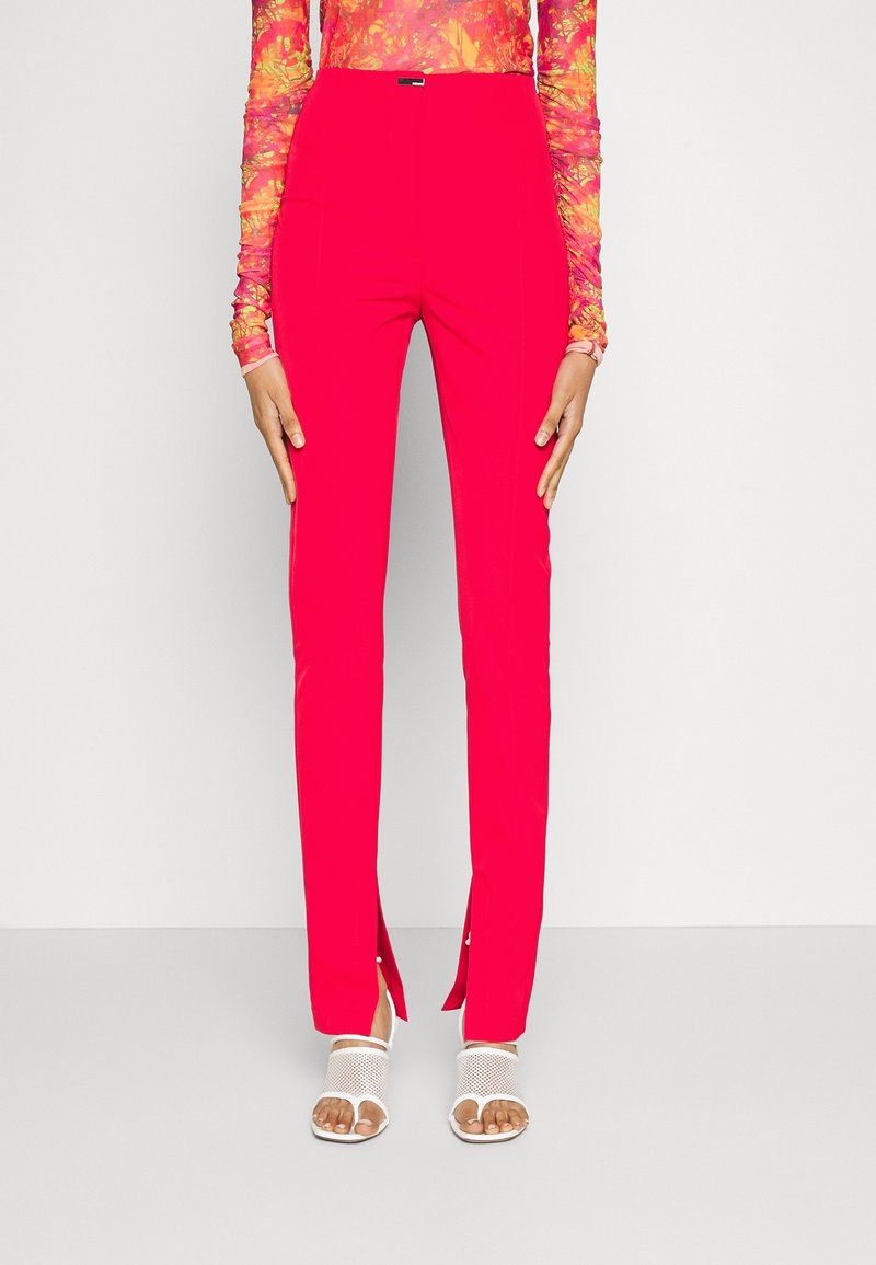 Pantalons ajustés taille haute en tissu rouge vif avec des fentes sur les côtés au bas. Associés à des sandales blanches à bout ouvert avec des détails en maille.