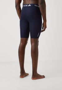 Shorts Techfit bleu marine avec une coupe ajustée, dotés d'une taille élastique et d'un branding blanc minimaliste sur le côté inférieur.