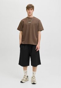 Brun bomulds t-shirt med korte ærmer, parret med sorte plisserede shorts. Iført cremede sokker og beige sneakers. Enkel sølv halskæde accent.