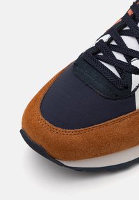 Nahk- ja tekstiilmaterjalist jooksuking, mille pealispind on pruun ja tumesinine, sisaldades valgeid detaile ja musti paelu. Tekstuuriga pind ja ümar varvaste kuju.