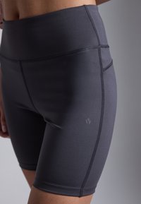 Shorts de sport taille haute en gris foncé, fabriqués à partir d'un tissu lisse et extensible. Présentent des coutures plates et un petit logo discret sur le côté.