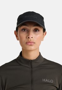 Czarna czapka z daszkiem z wytłoczonym logo "HALO". Osoba nosi również ciemnoszary, zapinany na zamek sweter o gładkiej fakturze i minimalistycznym designie.