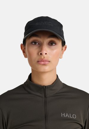 Svart basebollkeps med präglad "HALO"-logotyp. Bäraren har också på sig en mörkgrå zip-up-tröja med en slät textur och en minimalistisk design.