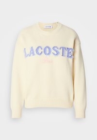 Κρέμα πουλόβερ με στρογγυλή λαιμόκοψη, ριμπ μανσέτες και στρίφωμα. "LACOSTE" σε φουντωτή μπλε γράμματα και "Παρίσι" σε απαλό ροζ κεντραρισμένα μπροστά.