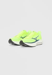 Αθλητικά παπούτσια σε λαχανί χρώμα με άνω μέρος από διαπνέον πλέγμα, μαύρη λαστιχένια σόλα και μπλε λεπτομέρειες στην πλευρά για επιπλέον σχεδιαστικό στοιχείο.