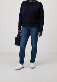 Laivastonsininen neule, jossa on teksturoitu neulekuvio, slim-fit tummat farkut, valkoiset lenkkarit, joissa on kumipohja, ja pieni laivastonsininen laukku.