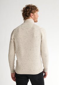 Maglione beige chiaro con un alto colletto, polsini a coste e un motivo a maglia testurizzato e variegato. Design semplice con una silhouette aderente.