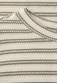 Nærbillede af creme- og grønstribet strikket stof med et tekstureret, løkkemønstret sting, der viser et foldet hjørne.