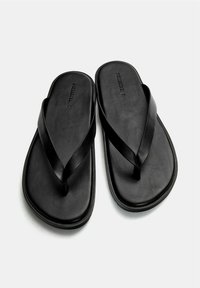 Infradito neri con una suola testurizzata e ampie cinghie lisce. Presentano un design elegante con una grafica minimale sulla soletta.