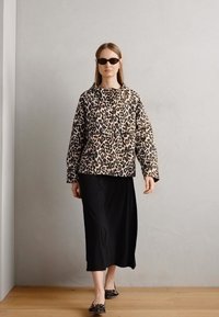 Geacă puffer cu imprimeu leopard și guler, asociată cu o fustă lungă neagră și pantofi negri fără toc, pe un fundal neutru.