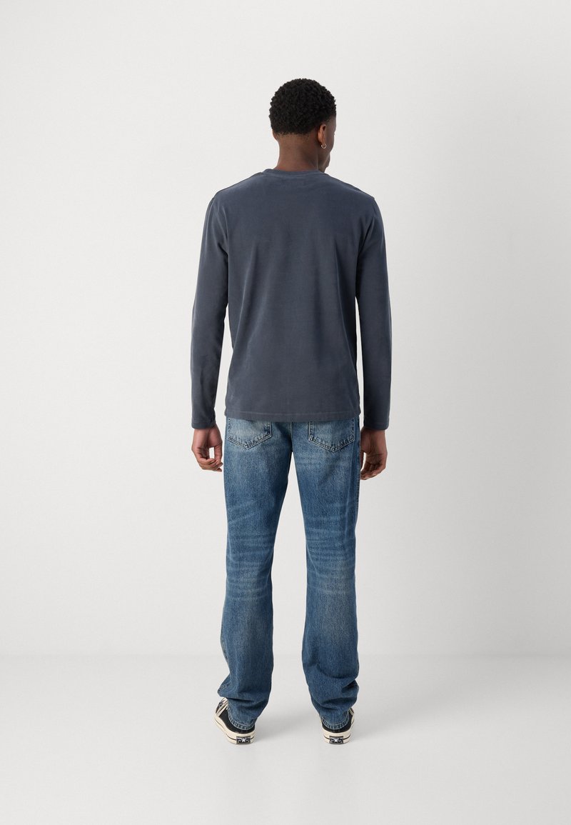 Langärmliges navyblaues Hemd aus weichem Material, kombiniert mit abgewetzten blauen Jeans und schwarzen Sneakern. Minimalistisches Design ohne sichtbare Logos.