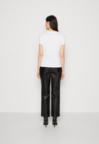 T-shirt bianco a maniche corte con scollatura rotonda, abbinato a pantaloni in pelle nera a vita alta e tacchi neri, visto da dietro.