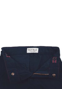 Laivastonsiniset housut, joissa on valkoinen "Band of Rascals" -label, punaiset tikkausteen ja sivutaskut, sekä kuparinvärinen vetskari. Teksturoitu puuvillakangas.