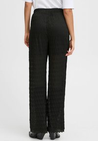 Zwarte kanten wijde broek met een elastische tailleband, voorzien van een gestructureerd bladenpatroon en een gegolfde zoom. Lichtgewicht, semi-doorzichtige stof.