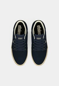 Baskets bleu marine avec une tige en daim, semelle en caoutchouc beige et lacets assortis. Marque "etnies" sur la languette et la semelle intérieure, design minimaliste.