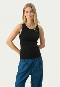Schwarzes, geripptes Tanktop mit runder Ausschnitt, kombiniert mit lockeren, blauen Denim-Hosen. Der Stoff wirkt weich mit einem leichten Glanz.