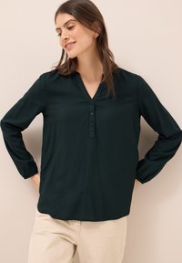 Dunkelgrünes Langarmshirt mit V-Ausschnitt, ausgestattet mit einer Knopfleiste und elastischen Bündchen. Glattes Material mit lockerer Passform.