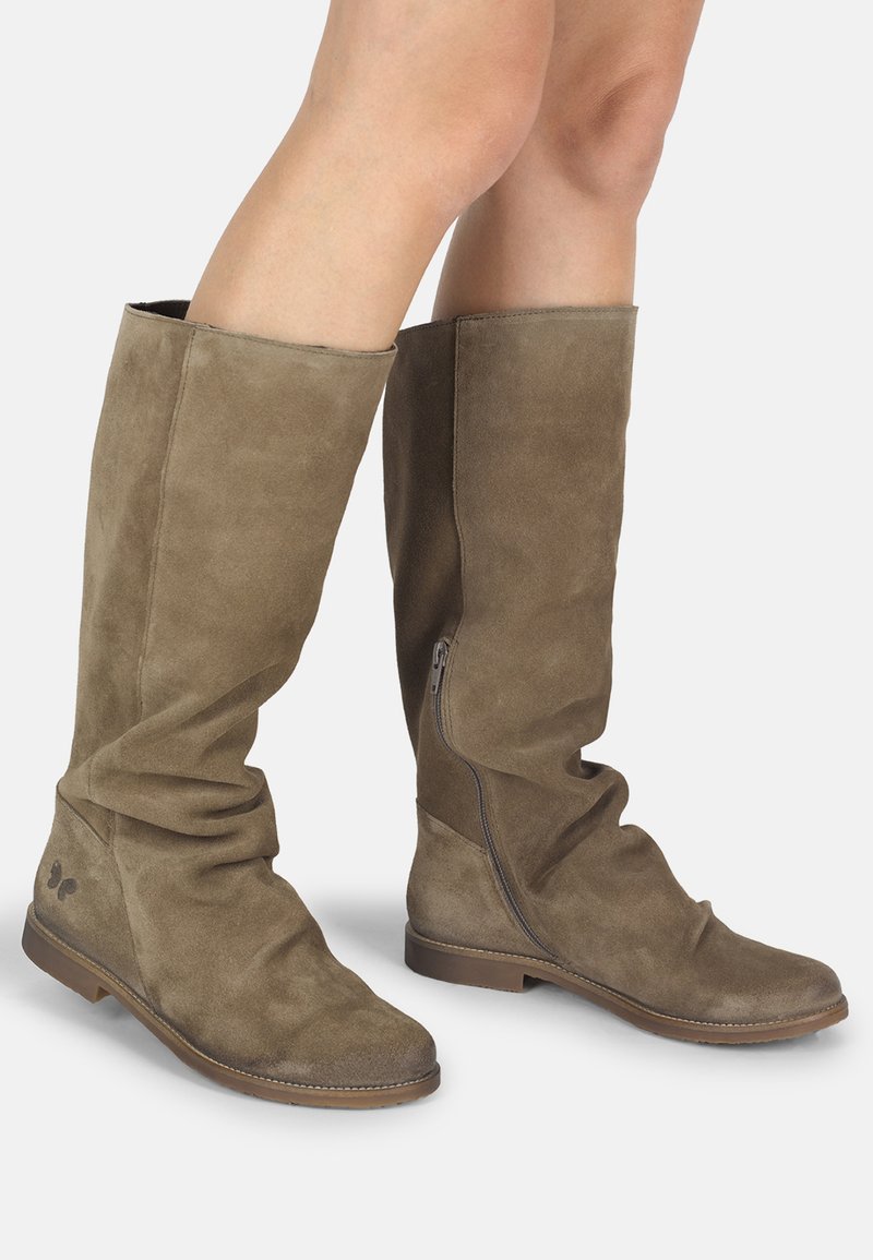 Bottes en daim brun jusqu'aux genoux avec des semelles plates et des fermetures éclair sur le côté, portées sur des jambes nues, montrant un léger froissement sur le matériau.