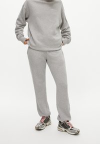 Felpa grigia con pantaloni della tuta abbinati in tessuto morbido. Logo notevole in grigio chiaro. Indossa sneakers con motivo e accenti multicolori.