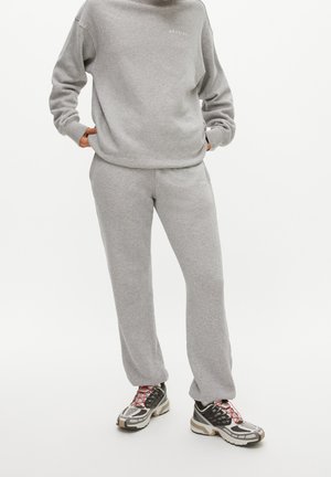Felpa grigia con pantaloni della tuta abbinati in tessuto morbido. Logo notevole in grigio chiaro. Indossa sneakers con motivo e accenti multicolori.
