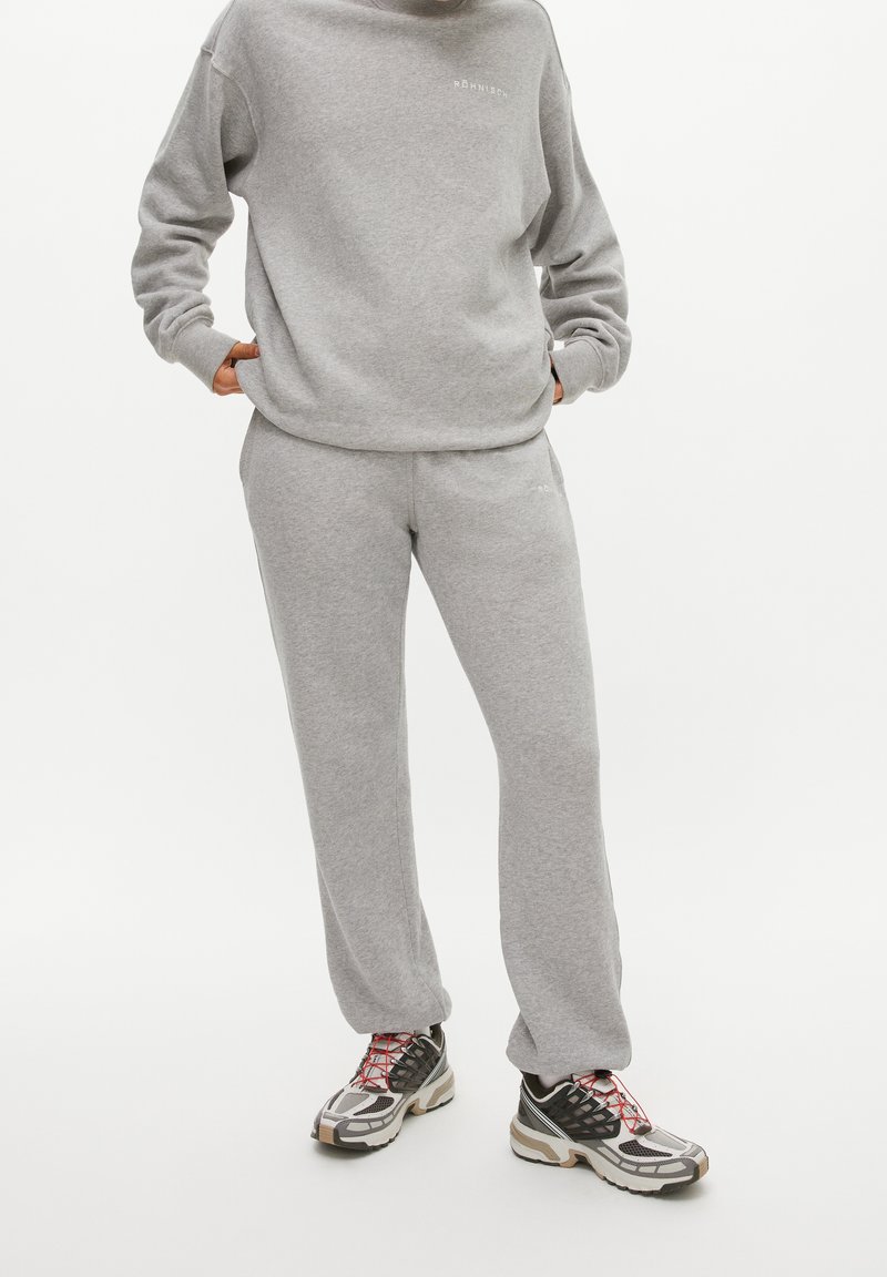 Felpa grigia con pantaloni della tuta abbinati in tessuto morbido. Logo notevole in grigio chiaro. Indossa sneakers con motivo e accenti multicolori.