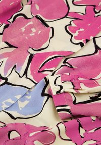 Bloemenstof met grote roze en blauwe bloemen op een crèmekleurige achtergrond. De textuur is glad, met zwarte omrandingen en een knoopdetail.