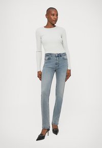 Camisola de mangas longas cinza claro combinada com jeans azul de corte slim. Os jeans apresentam um design clássico de cinco bolsos e detalhes subtis. Saltos altos pretos.