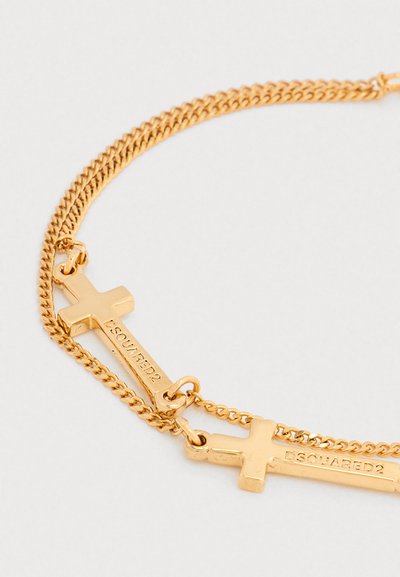 Bracelet chaîne en or avec deux pendentifs croix horizontaux gravés de "DSQUARED2" sur un fond blanc.