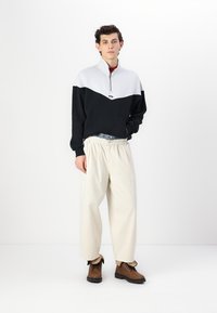 Svart och vit kvartshalsad tröja, lös passform på krämfärgade byxor och bruna snörskor. Bekväma material i bomullsblandning.