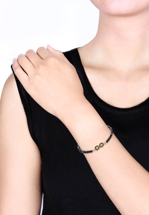 Sort perlearmbånd med et guld uendelighedstegn med detaljeret udsmykning, båret på en bar arm.