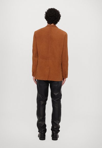 Brown suede jacket with a tailored fit, featuring a stand collar and two-button cuffs, paired with black leather pants and boots.